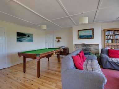 A room with a pool table a stone fireplace two grey sofas with red cushions and a bookshelf at Waterson in Osmington