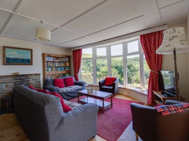 A living room with gray sofas and red cushions a wooden coffee table a bookshelf a large window with red curtains and a floor lamp at Waterson in Osmington