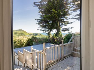 A view through a window of a wooden deck and railing with trees and hills in the background at Waterson in Osmington