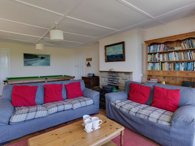 A living room with two sofas with red cushions a wooden coffee table with mugs a bookshelf and a fireplace at Waterson in Osmington
