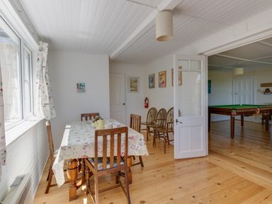 A dining area with wooden chairs and a table covered with a tablecloth next to windows and an open door leading to a room with a pool table at Waterson in Osmington