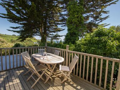 A wooden deck with a wooden table and four chairs surrounded by trees and greenery at Waterson in Osmington