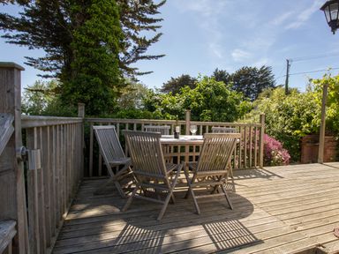 A wooden deck with a round table and five wooden chairs surrounded by greenery at Waterson in Osmington