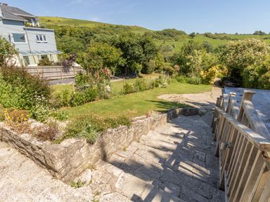 Stone steps with wooden railing leading down to a garden with grass trees and bushes near a house at Waterson in Osmington