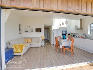 An open living space with a sofa, dining table, chairs, and kitchen appliances at The Wave in Eype