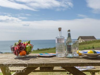 A wooden picnic table with a bowl of fruit plates bottles and glasses by the sea at The Wave in Eype