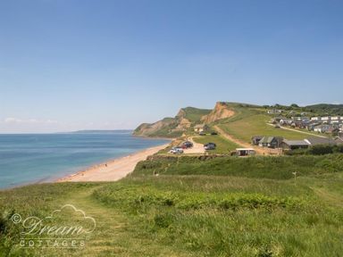 A coastal landscape with grassy hills a sandy beach parked cars and buildings at The Wave in Eype
