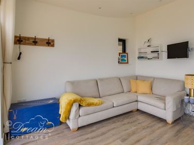 A corner living room with a beige sofa yellow cushions a blue chest a wall-mounted tv and shelves at The Wave in Eype