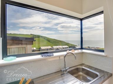 A kitchen sink with a faucet under a corner window showing a hillside and buildings at The Wave in Eype