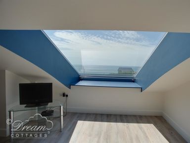 A room with a television on a glass stand and a large skylight window with an ocean view at The Wave in Eype