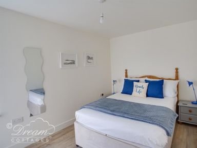 A bedroom with a double bed blue cushions a blue blanket two bedside tables two lamps a wavy mirror and two pictures on wall at The Wave in Eype