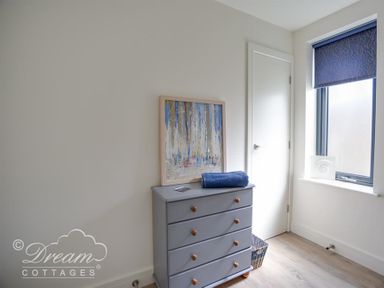 A gray chest of drawers with a painting and a blue towel on top next to a white door and window at The Wave in Eype