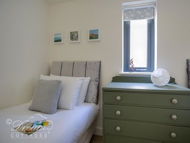 A bedroom with a single bed with pillows beside a green chest of drawers under a window at The Wave in Eype