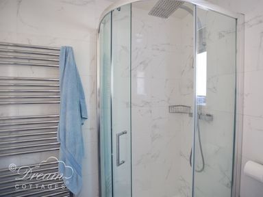 A bathroom with a glass shower enclosure a chrome towel rack with a blue towel and marble tiled walls at The Wave in Eype