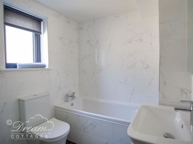 A bathroom with a bathtub toilet and sink with tiled walls at The Wave in Eype