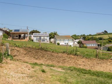 A row of small cottages on a grassy hill with a clear sky at The Wave in Eype