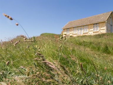 A cottage on a grassy hill under a blue sky at The Wave in Eype