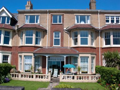 A view of a brick house with bay windows a small porch and a garden with outdoor furniture at Weymouth Bay Apartment B in Greenhill
