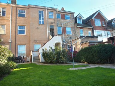 A backyard with a green lawn and bushes and a clothesline next to a brick apartment building Weymouth Bay Apartment B Greenhill