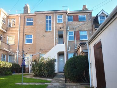 A backyard garden with green grass bushes a clothesline and brick houses at Weymouth Bay Apartment B in Greenhill