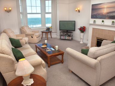 A living room with beige sofas green cushions a wooden coffee table a television and a window showing the sea at Weymouth Bay Apartment B in Greenhill