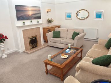 A living room with beige sofas and green cushions two cups and a plate on a wooden coffee table paintings on the wall at Weymouth Bay Apartment B in Greenhill