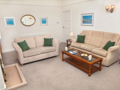 A living room with two beige sofas green pillows wooden coffee table and framed pictures at Weymouth Bay Apartment B in Greenhill