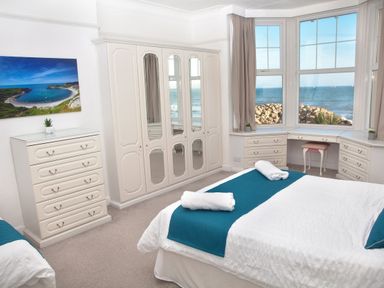 A bedroom with a bed two rugs a wardrobe chest of drawers and a desk by the window at Weymouth Bay Apartment B in Greenhill