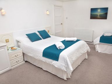 A bedroom with a double bed and a single bed both with teal runners and pillows at Weymouth Bay Apartment B in Greenhill