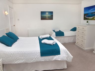A bedroom with two beds a chest of drawers and wall art at Weymouth Bay Apartment B in Greenhill