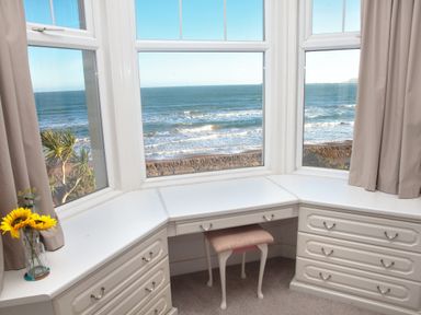 A white built-in desk with drawers and a chair by a bay window overlooking the ocean at Weymouth Bay Apartment B in Greenhill