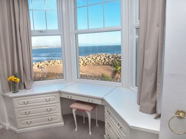 A corner desk with drawers and a stool by a bay window overlooking the sea at Weymouth Bay Apartment B in Greenhill