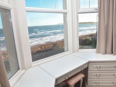 A white desk with drawers and a pink stool by a window overlooking the ocean at Weymouth Bay Apartment B in Greenhill