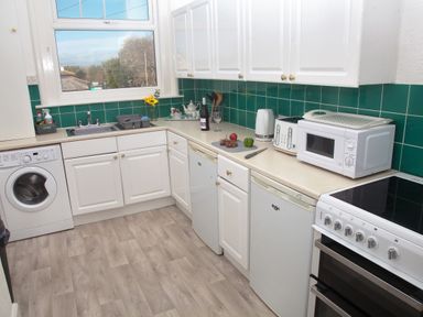 A kitchen with white cabinets cooking appliances and green tiled backsplash at Weymouth Bay Apartment B in Greenhill