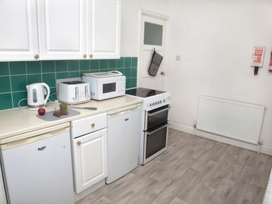 A kitchen with white cabinets green tiled backsplash appliances on the counter and a white stove at Weymouth Bay Apartment B in Greenhill