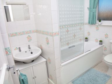 A bathroom with a sink cabinet bathtub with glass shower screen toilet and blue bath mat at Weymouth Bay Apartment B in Greenhill
