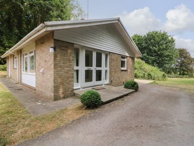 An exterior view of a single story brick house with white framed doors and windows and surrounding trees at Woodlands Cottage in Ringstead