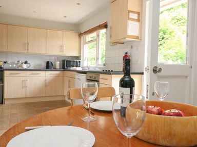 A kitchen with wooden cabinets a round wooden table set with plates glasses a bottle of wine and a bowl of apples at Woodlands Cottage in Ringstead