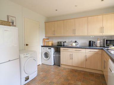 A kitchen with washing machine dryer refrigerator countertop microwave toaster kettle and cabinets at Woodlands Cottage in Ringstead
