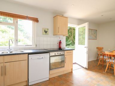 A kitchen with dishwasher oven sink open door and dining table with chairs at Woodlands Cottage in Ringstead
