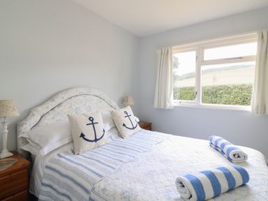 A bedroom with a bed with striped bedding two anchor pillows bedside tables with lamps and a window overlooking a garden at Woodlands Cottage in Ringstead