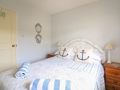 A bedroom with a bed with anchor pillows striped towels and wooden bedside tables with lamps at Woodlands Cottage in Ringstead