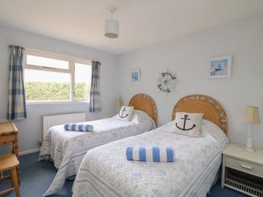 A bedroom with two single beds with wicker headboards striped towels and pillows with anchors at Woodlands Cottage in Ringstead