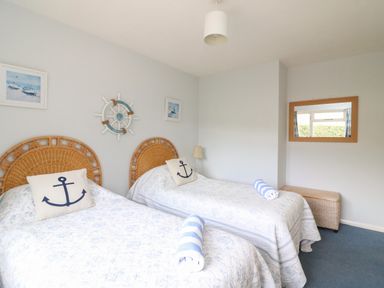 A bedroom with two single beds each with an anchor cushion and rolled towels above a wicker bench with a wall mirror at Woodlands Cottage in Ringstead