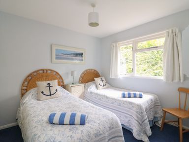 A bedroom with two single beds with anchor pillows and blue striped towels by a window with white curtains at Woodlands Cottage in Ringstead