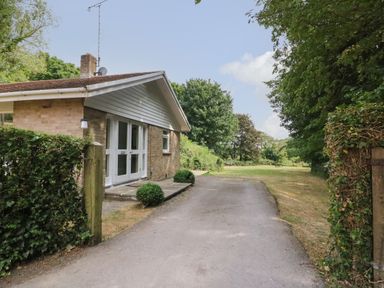 A driveway leading to a brick house with white doors and hedge on the side at Woodlands Cottage in Ringstead