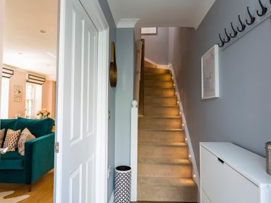A hallway with carpeted stairs lit by small lights and a glimpse of a living room with a teal sofa at 16 Courtenay Street Salcombe