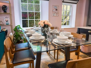 A dining room with a glass table set with plates bowls glasses and chopsticks with wooden chairs around the table at 16 Courtenay Street in Salcombe
