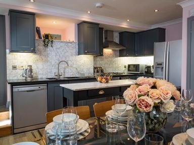 A kitchen with dark cabinets a marble island and a dining table with a flower vase at 16 Courtenay Street Salcombe