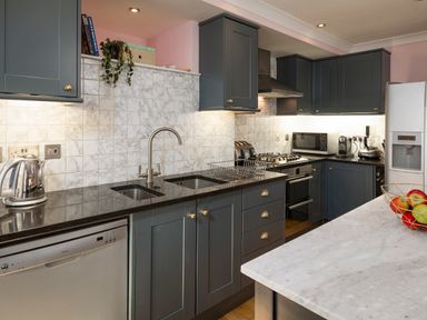 A kitchen with dark cabinets stainless steel appliances and a fruit bowl on a marble countertop at 16 Courtenay Street in Salcombe